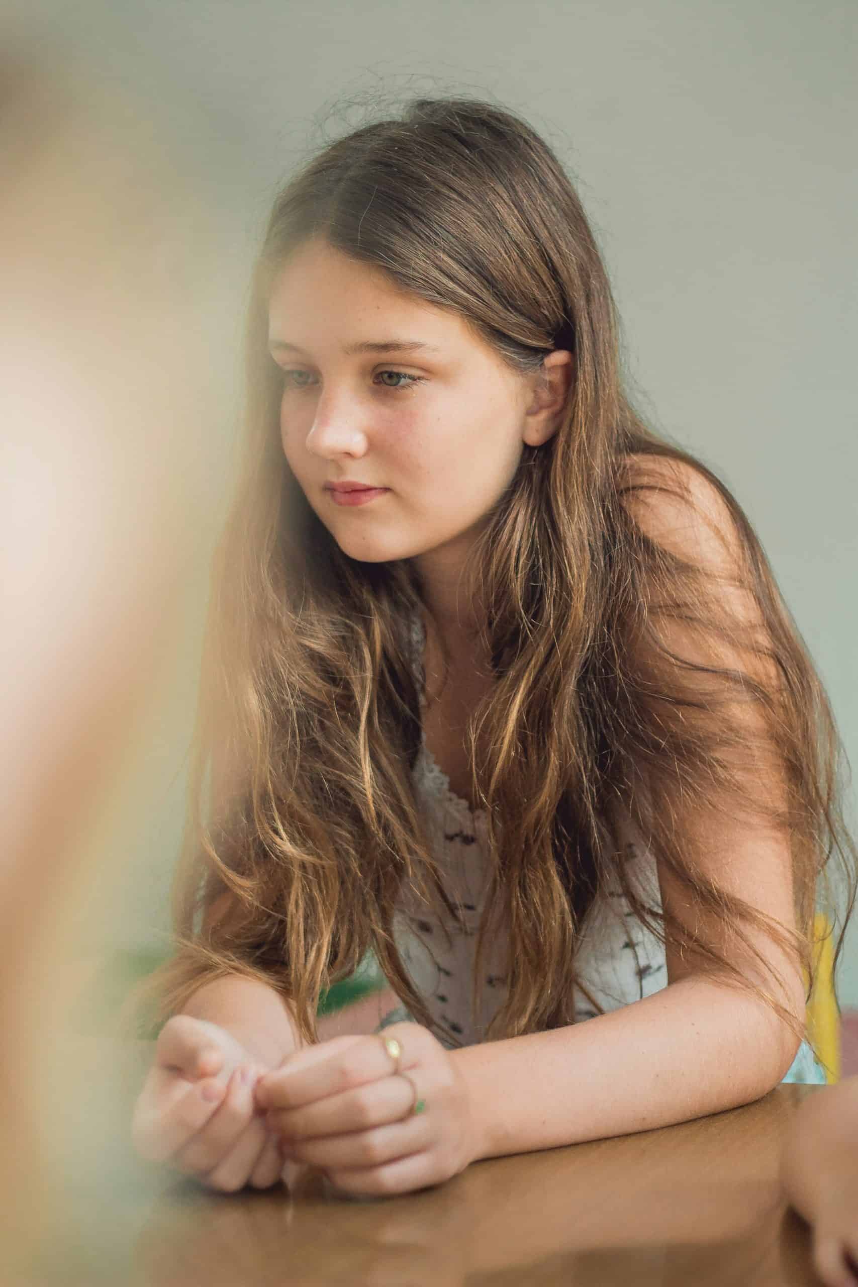 Close-up of a young girl with long brown hair, contemplating in an educational therapy environment.